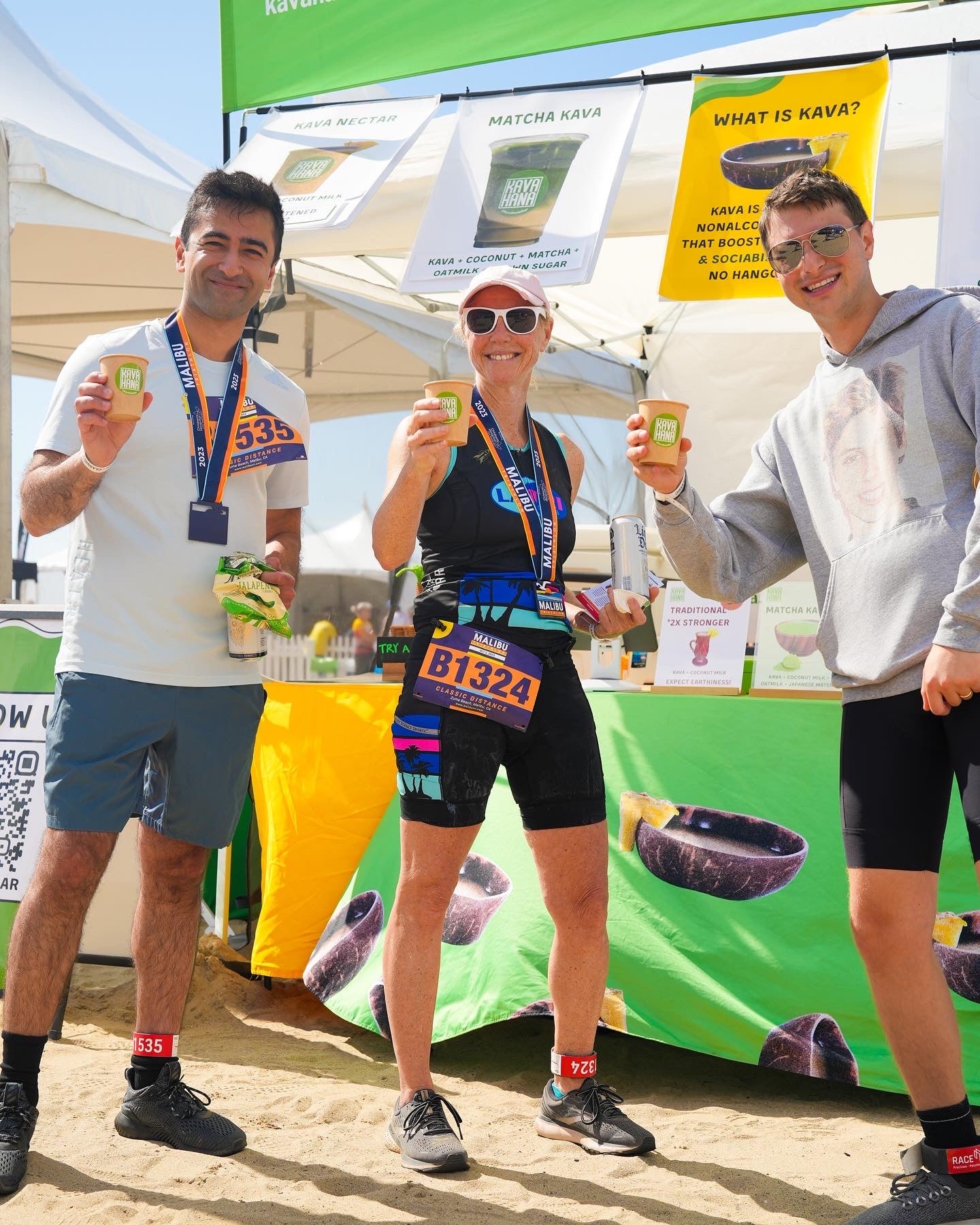 A photograph depicting 3 happy people enjoying kava nectar as a beverage on the beach during the sunny day at the malibu triathlon