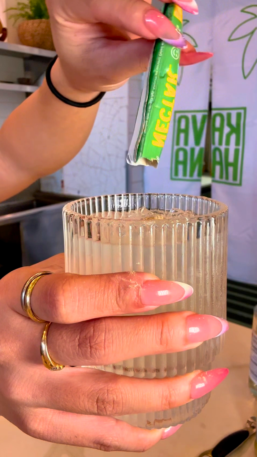 Pouring a Kava Nectar stick pack into a ribbed glass of iced Kava Nectar Scowl Mule mocktail. 
