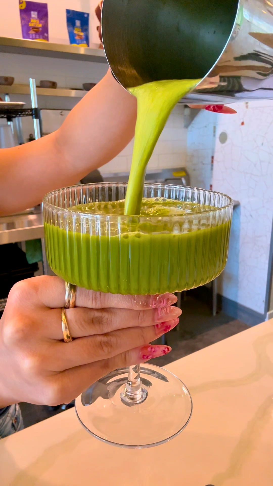 Pouring a Matcha Kava Nectartini Mocktail from a shaker into a ribbed coupe glass at the Kavahana bar. 