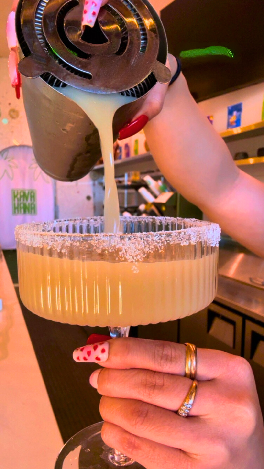 Straining a Lemon Drop Kava Nectar Shot Mocktail from a shaker into a sugar-rimmed coupe glass. 