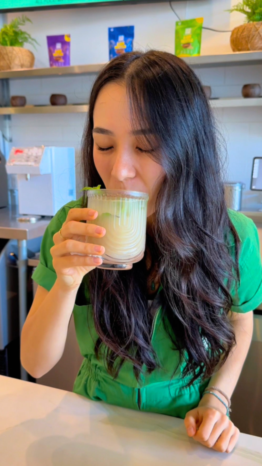 Drinking a Kava Nectar Apple Ginger Fizz over ice, garnished with fresh mint, in front of the Kava Nectar shelf at the Kavahana bar.