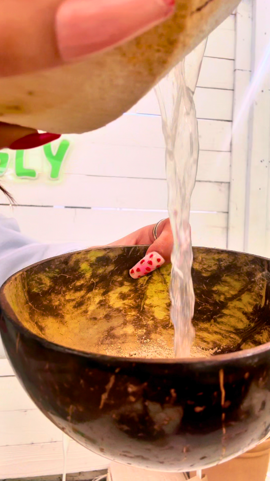 Coconut water being poured over Kava Nectar powder in a traditional coconut shell bowl to make OG Kava Nectar. 