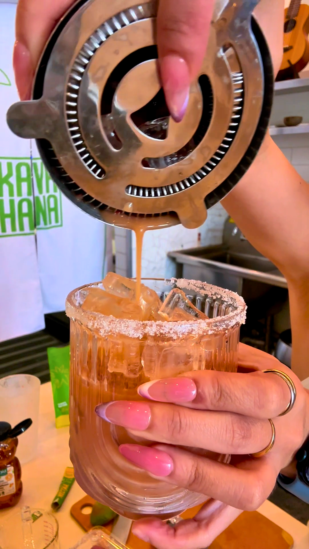 Strawberry Lime Kavarita mocktail being strained into a salt-rimmed glass of ice, with a Kava Nectar stick pack on the counter.
